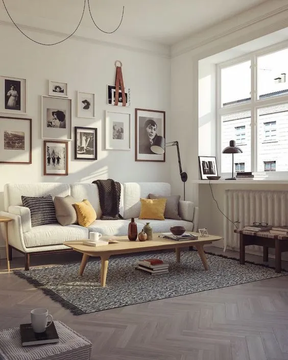 Bright living room with white sofa, wooden coffee table, gallery wall, patterned rug, and windows