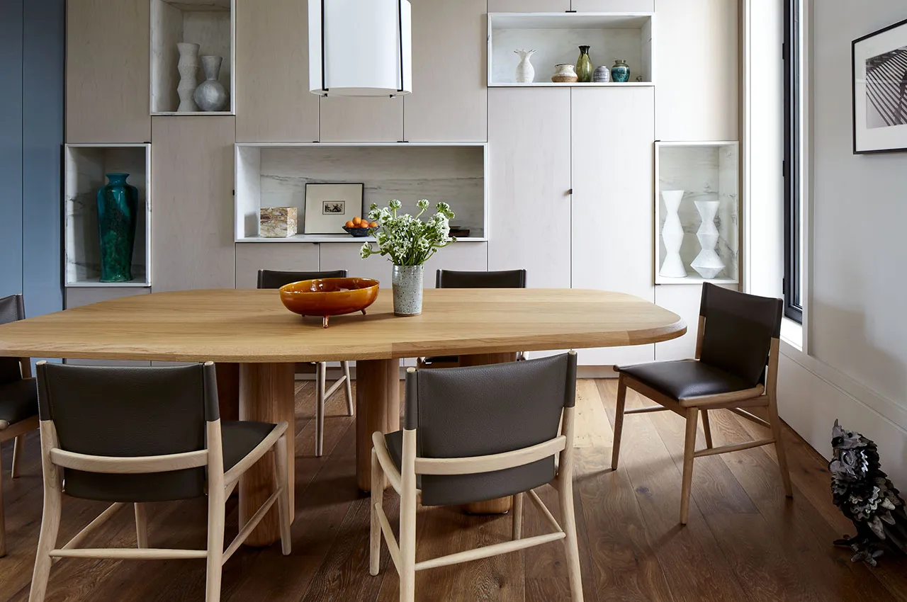 Oval wood dining table with dark chairs and white storage wall featuring various decorative vases