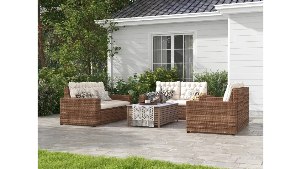 Brown wicker outdoor furniture with white cushions and wooden coffee table on backyard stone patio