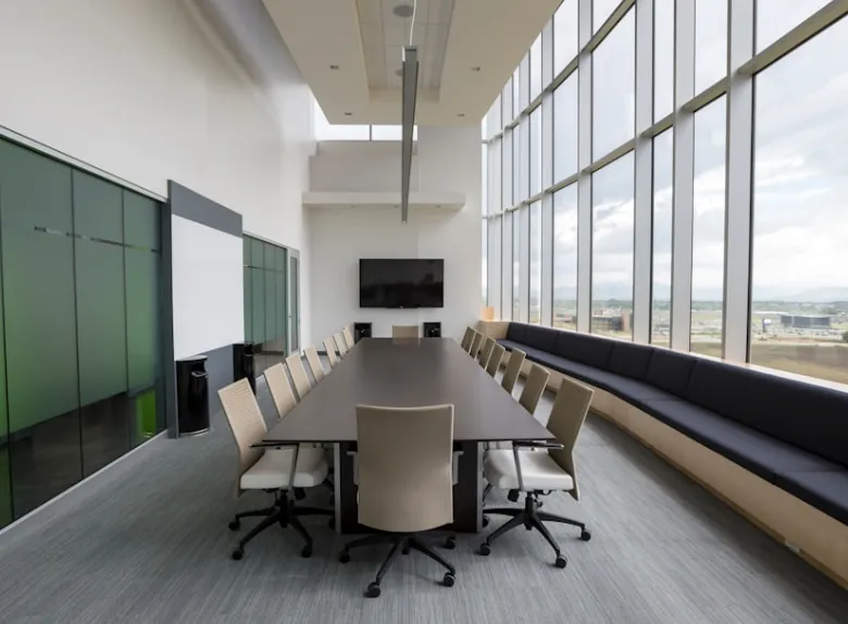 Modern office meeting room with long dark table chairs large windows and wall mounted television