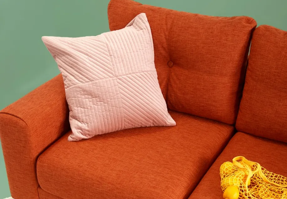 Orange sofa with pink patterned pillow and yellow net bag filled with fresh yellow lemons